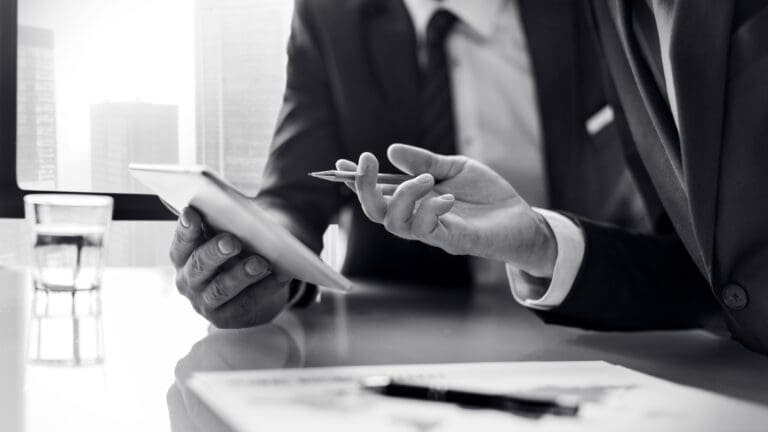 Close-up of two business professionals in suits discussing financial documents and data on a tablet
