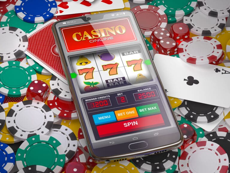Smartphone displaying an online casino slot machine game with triple sevens on the screen, surrounded by colorful poker chips, dice, and playing cards.
