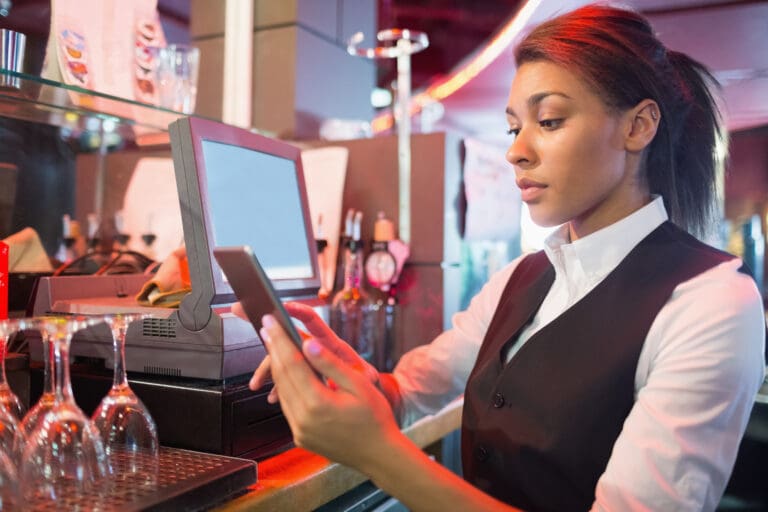 A casino hospitality staff member using a mobile device at a bar service station.